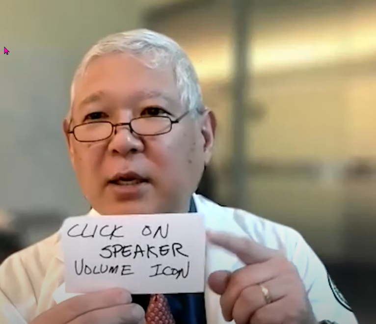 Dr. Sato acting in video on zoom telehealth and holds up sign to screen 